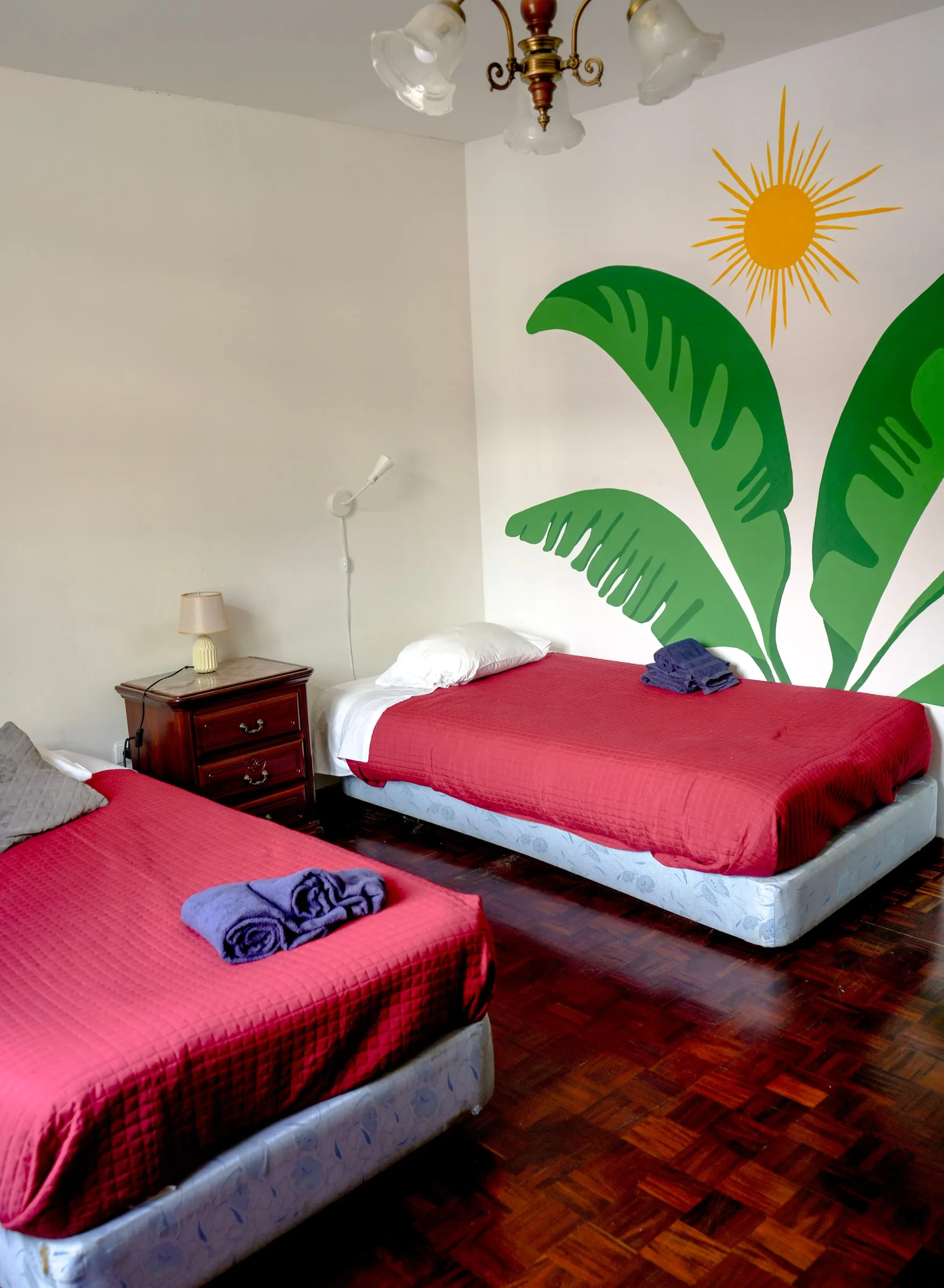 Penne twin beds with red covers and a banana-leaf mural